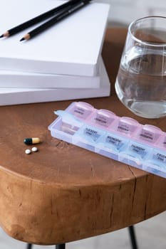 Closeup of medical pill box with doses of tablets for daily take a medicine and glass of water