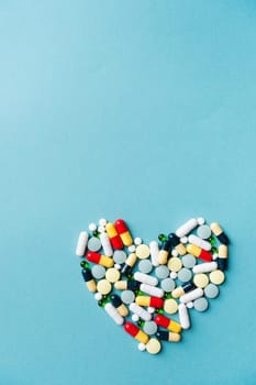 Pills forming heart shape on blue background, copy space