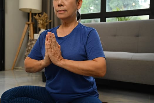 Peaceful senior practicing yoga at home. Wellness and mental health balance concept