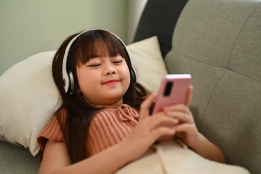 Happy asian child girl watching children content in social networks on mobile phone.