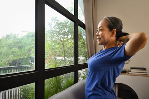 Happy retired woman in sportswear doing stretching exercises at home. Sports and Healthy lifestyle concept