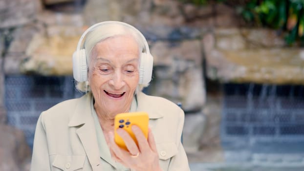 Happy senior woman listening to music with headphones and mobile outdoors of a geriatric