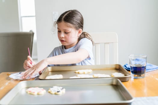 A heartwarming scene of a little girl carefully writing 'Sorry' on sugar cookies with food coloring, the cookies beautifully flooded with white royal icing.