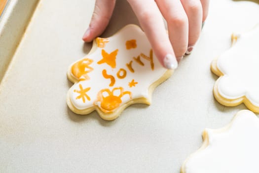 A heartwarming scene of a little girl carefully writing 'Sorry' on sugar cookies with food coloring, the cookies beautifully flooded with white royal icing.