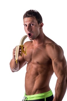 Handsome muscular shirtless man eating banana, isolated on white in studio, looking at camera