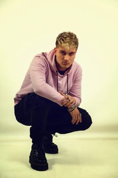 Attractive blond young man with blue eyes, wearing pink sweater, in studio shot on neutral background