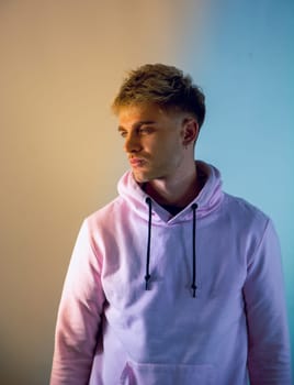 Attractive blond young man with blue eyes, wearing pink sweater, in studio shot on neutral background