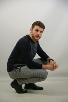Attractive young man with blue eyes, wearing black elegant sweater, in studio shot on neutral background