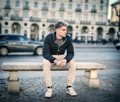 Attractive young man in urban environment, sitting on bench in Turin, Italy