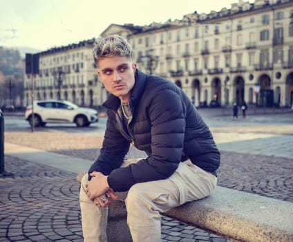 Attractive young man in urban environment, sitting on bench in Turin, Italy