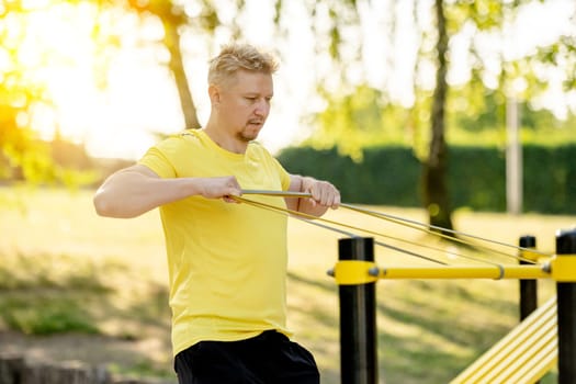 Man doing push ups with horizontal bar outdoors in park for healthy wellbeing. Sportsman guy making strong workout for muscle