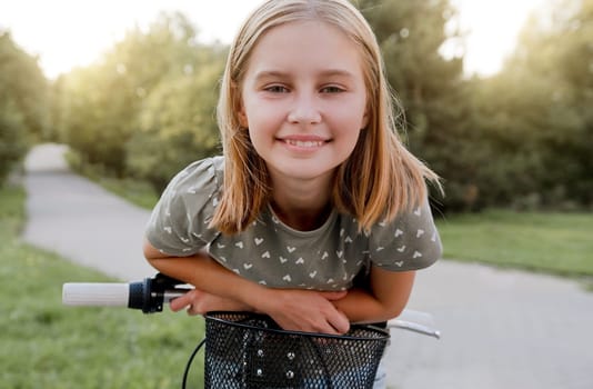 Cute preteen girl with bycicle outdoors looking at camera and smiling. Pretty child with bike at city street at summer park