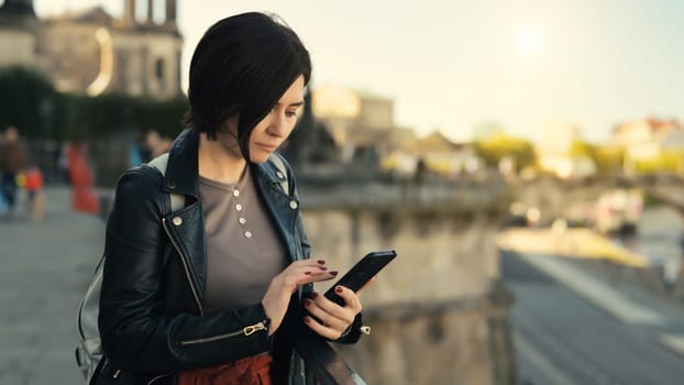 Young Woman Reads Smartphone Against Blurred City Backdrop In Autumn