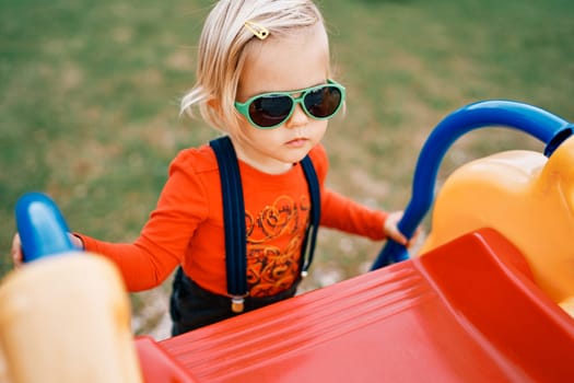 Little girl in sunglasses climbs a slide holding onto the handrails. High quality photo