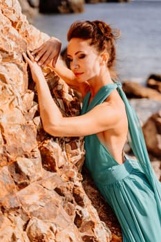 Woman green dress sea. Woman in a long mint dress posing on a beach with rocks on sunny day. Girl on the nature on blue sky background