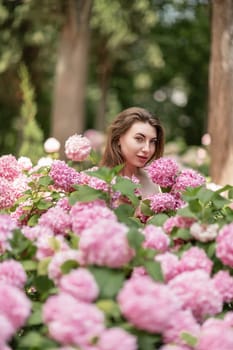 Hydrangeas Happy woman in pink dress amid hydrangeas. Large pink hydrangea caps surround woman. Sunny outdoor setting. Showcasing happy woman amid hydrangea bloom