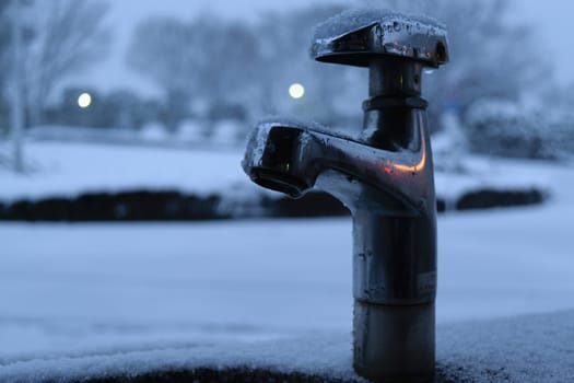 A faucet covered in ice set against a snowy backdrop
