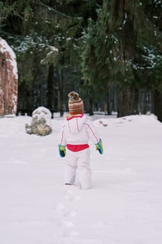Little girl walks through deep snow towards a coniferous forest. Back view. High quality photo