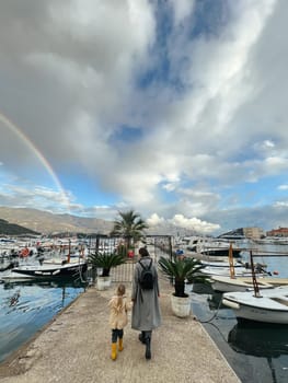 Mom with a little girl walk along the pier against the backdrop of a rainbow over the mountains. High quality photo
