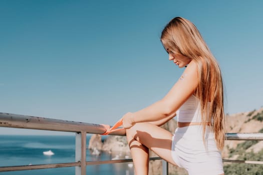 Young woman with black hair, fitness instructor in pink sports leggings and tops, doing pilates on yoga mat with magic pilates ring by the sea on the beach. Female fitness daily yoga concept