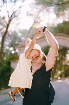 Dad lifts a little girl by the arms high and kisses her on the cheek. High quality photo