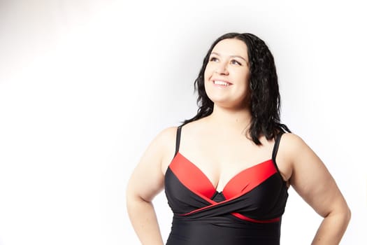 Portrait of attractive dreamy thick woman in red black swimsuit posing on white background. Body positive, photoshoot, selfie. Funny plus size model