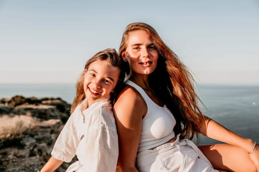 Close up portrait of mom and her teenage daughter hugging and smiling together over sunset sea view. Beautiful woman relaxing with her child.