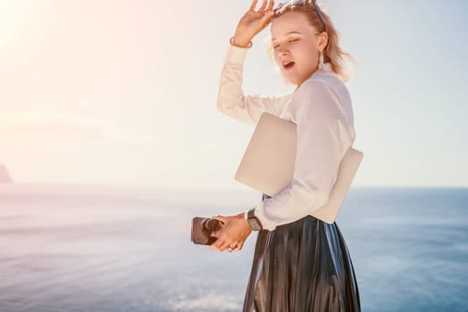 Digital nomad, Business woman working on laptop by the sea. Pretty lady typing on computer by the sea at sunset, makes a business transaction online from a distance. Freelance remote work on vacation