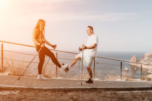 Happy Middle aged couple or friends practicing nordic walking in park near sea. Mature couple with trekking poles walking, practicing Nordic walking outdoors. Aging youthfully and sport concept.