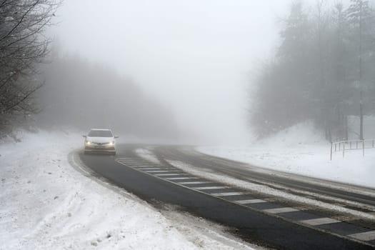 Cars in the fog. Bad winter weather and dangerous automobile traffic on the road. Light vehicles in foggy day.