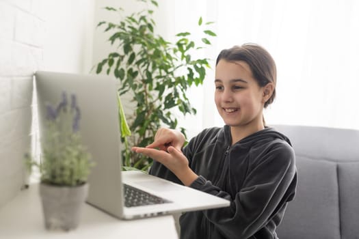 A teenage girl sits in front of her laptop learning sign language, a language for the deaf online.