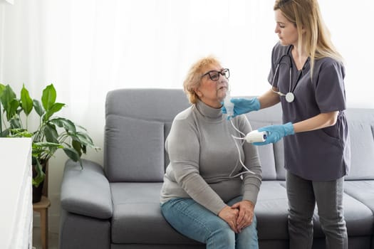 Young girl doctor makes inhalation to an older woman on a white background. Fight nasal congestion and rhinitis