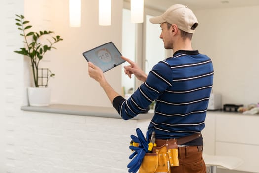 electrician in hardhat and safety vest holding digital tablet and fixing electric panel.