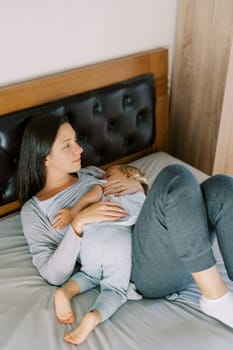 Mom breastfeeds a little girl lying on her stomach on the bed. High quality photo