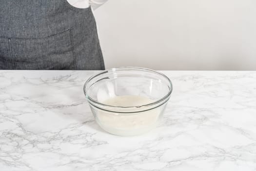 Mixing ingredients in a large glass mixing bowl to make homemade royal icing.