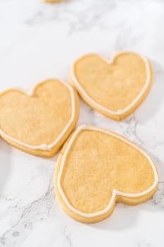 Decorating heart-shaped sugar cookies with pink and white royal icing for Valentine's Day.