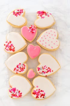 Storing heart-shaped sugar cookies with pink and white royal icing in a large plastic container.
