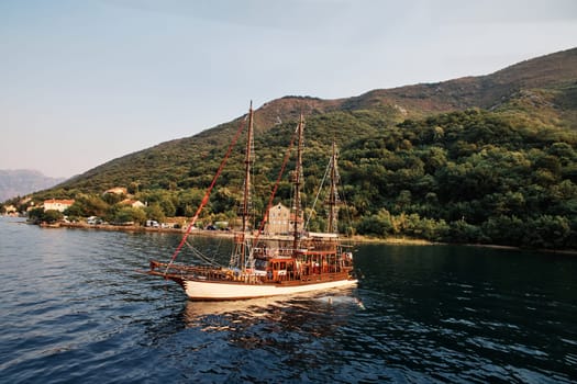 Wooden schooner sails on the sea against the background of a mountainous coast. Drone. High quality photo