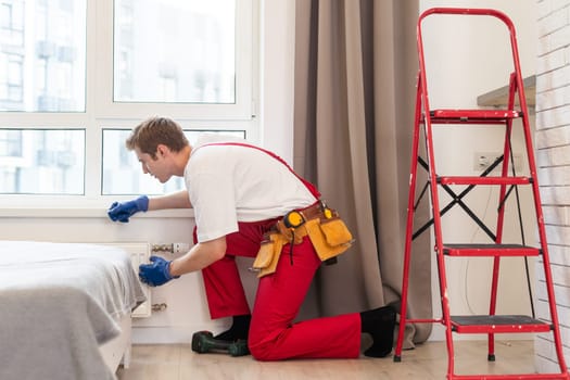 A plumber is fixing a radiator. With an adjustable wrench, he tightens the tap. A briefcase with a tool at hand.