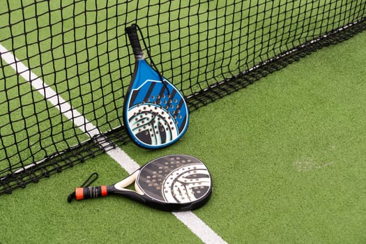 Yellow balls on grass turf near padel tennis racket behind net in green court outdoors with natural lighting. Paddle is a racquet game. Professional sport concept with copy space. High quality photo