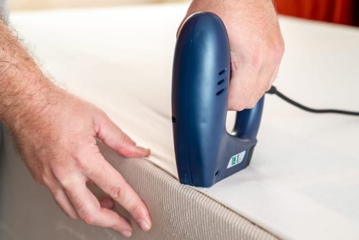 Worker stapling sofa lining with electric staple gun