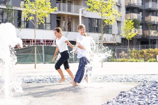 Happy teenage girl dancing in a fountain in a city park on a hot summer day. High quality photo