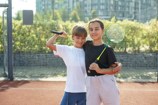 Happy sporty elementary school age girl, child playing badminton, holding a racket making funny faces, portrait, lifestyle. Sports, exercise and healthy outdoor activities leisure concept, one person. High quality photo