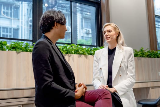 Caucasian business woman sit and discuss with her Asian coworker during break or relax time in coworking space of the company.