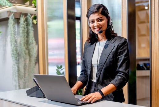Portrait of Asian business woman wear headphone work with laptop look like customer service stand and look at camera with smiling.