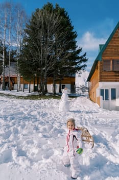 Little girl with a sled on a rope goes down the hill past a snowman. High quality photo