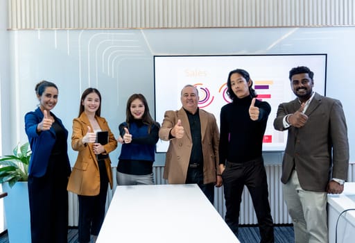 Portrait of Caucasian and Asian business men and women show thumbs up and smile to camera in area of conference or meeting room in office.