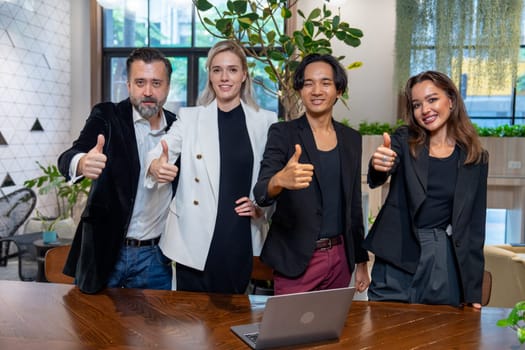 Portrait of Caucasian and Asian business men and women show thumbs and smile to camera in area of coworking space in office.