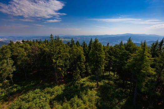 Beautiful green and blue panorama of layers of mountains and trees and some fields seen from top of viewing tower at highest mountain in this area