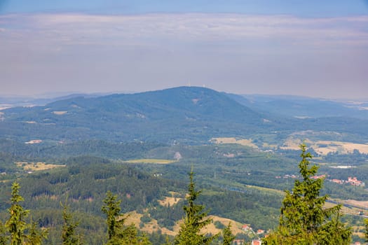 Beautiful green and blue panorama of layers of mountains and trees and some fields seen from top of viewing tower at highest mountain in this area